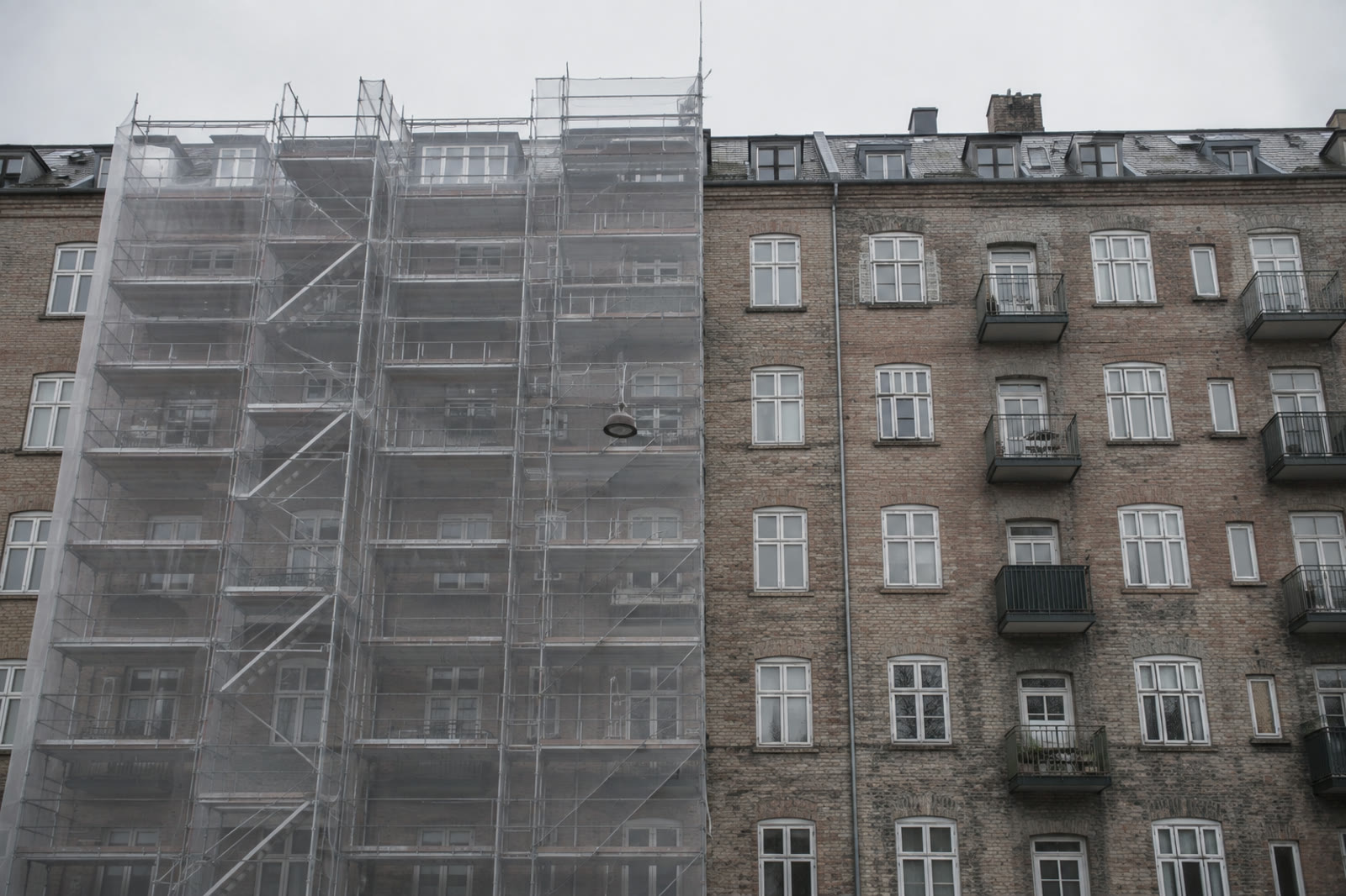 Stillads med net foran en facade, nabohuset står færdigt ved siden af